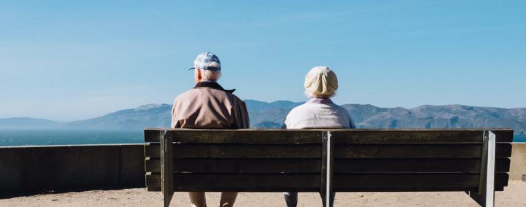 elderly couple sitting on bench with mountain view