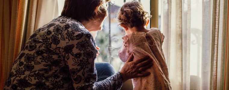 grandmother looking out a window with her arm around her granddaughter